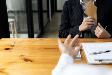 A person is putting money envelope in a suit pocket, she is a company employee in charge of a large project and receives bribes from competitors in exchange for project information. Bribery concept.の写真素材