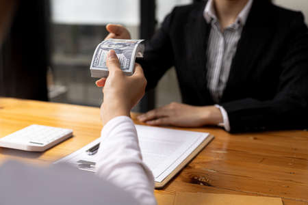 Two people are handing each other dollar bills, they are mutually beneficial business partners, they...