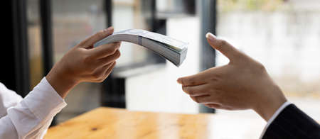 Two people are handing each other dollar bills, they are mutually beneficial business partners, they commit bribery fraud for business interests. The concept of corruption and bribery.の写真素材