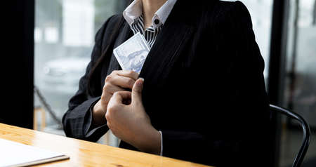 A person is putting money in a suit pocket, she is a company employee in charge of a large project and receives bribes from competitors in exchange for project information. Bribery concept.の写真素材