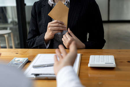 A person is putting money envelope in a suit pocket, she is a company employee in charge of a large project and receives bribes from competitors in exchange for project information. Bribery concept.の写真素材