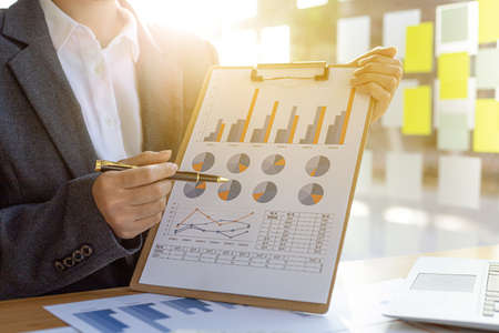 Finance staff holding financial graph documents presented to executives and attendees via...