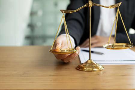 The lawyer puts a second hand on the scales of justice on his desk, stating that the matter must be justified and not contrary to law and humanity. The concept of legal jurisprudence.の写真素材