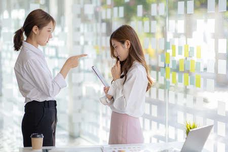 Two women were standing talking, the department head was blaming and warning a female employee who had made a mistake, causing the effect to many parties. Called to blame. Error working concept.の写真素材