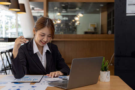 A beautiful Asian businesswoman sitting in her private office, she is checking company financial documents, she is a female executive of a startup company. Concept of financial management.の写真素材