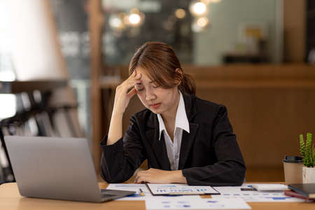 Beautiful Asian woman working in an office, she is a businesswoman who owns a company, she has a headache due to long and large paperwork leaving her tired and dizzy. The concept of sickness from workの写真素材