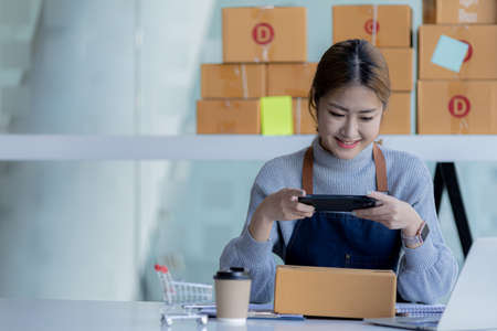 A woman using a smartphone to take pictures in front of parcel boxes, parcel boxes for packing...