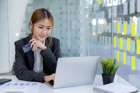 Beautiful woman holding a credit card, she uses a credit card to pay for goods and services online,...