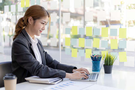 Beautiful Asian young woman looking at information on a laptop, concept image of Asian business...