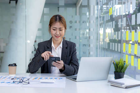 young businesswoman looking at financial information from a mobile phone, she is checking company financial documents, she is a female executive of a startup company. Concept of financial management.の写真素材