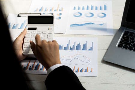 Business women using a calculator to calculate numbers on a company's financial documents, he is...