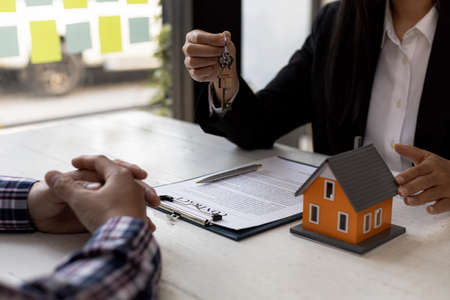 A home rental company employee is handing the house keys to a customer who has agreed to sign a rental contract, explaining the details and terms of the rental. Home and real estate rental ideas.の写真素材