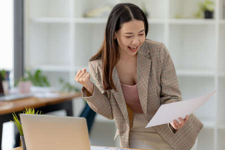 Woman gesturing and looking at the document, businesswoman checking company monthly sales and pretending to be happy as sales meet planned targets according to policy. Sales management concept.の写真素材