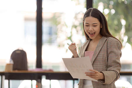 Woman gesturing and looking at the document, businesswoman checking company monthly sales and pretending to be happy as sales meet planned targets according to policy. Sales management concept.の写真素材