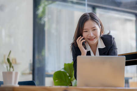 Asian woman talking on the phone, she is a salesperson in a startup company, she is calling customers to sell products and promotions. Concept of selling products through telephone channels.の写真素材