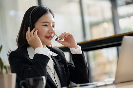 Beautiful Asian woman, she is a call center employee of an Internet and telephone company, she is responsible for providing service and assistance to customers through the phone. Call center concept.の写真素材