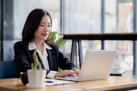 Beautiful Asian young woman looking at information on a laptop, concept image of Asian business woman working smart, modern female executive, startup business woman, business leader woman.の写真素材
