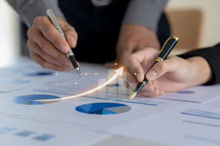 Two businessmen are meeting together, they point to financial documents to discuss plans and solutions, chart graphics showing financial status and performance. Business administration concept.の写真素材