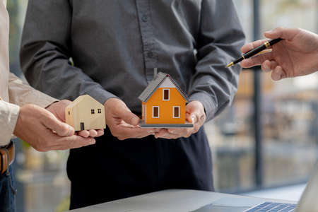 A person standing holding a miniature house model, presents a housing project in the project to bid for a construction concession. The concept of building a housing project.の写真素材