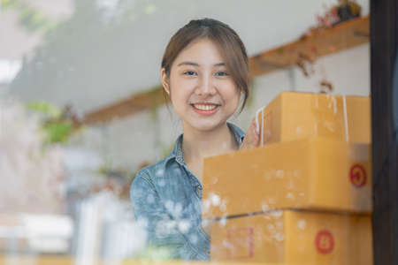 A beautiful Asian business owner opens an online store, she is checking orders from customers, sending goods through a courier company, concept of a woman opening an online business.の写真素材