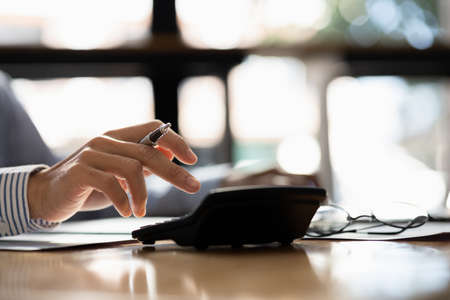 Close-up of a business man using a white calculator, a financial businessman examining the numerical data on a company financial document, he uses a calculator to verify the accuracy of numbers.の写真素材