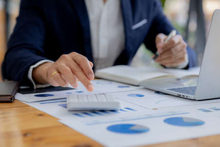 Close-up of a business man using a white calculator, a financial businessman examining the numerical data on a company financial document, he uses a calculator to verify the accuracy of numbers.の写真素材
