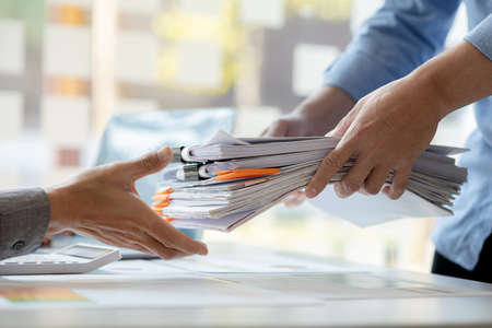 A male office worker is bringing a pile of financial documents to the head of the finance department...