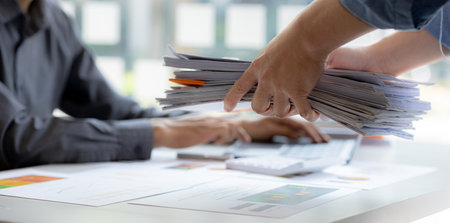 A male office worker is bringing a pile of financial documents to the head of the finance department to verify the correctness of the information before attending a meeting with the management.の写真素材