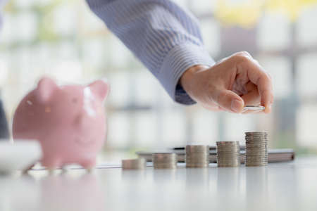 business man is stacking coins on top of the coin pile on the highest row. Placing coins in a row...