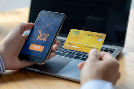 A person is holding a credit card to pay online, credit card payments can be used on both laptop...