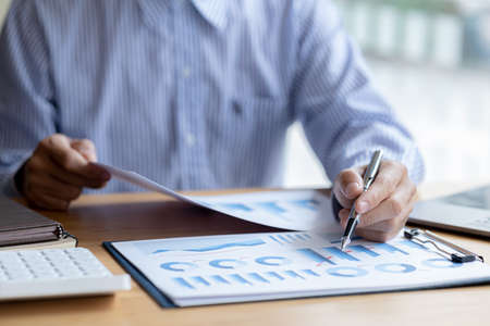 Businessman check to financial documents, he owns a startup company, he sits checking the company's financial summary prepared by the finance department. Management concept of startup company.の写真素材