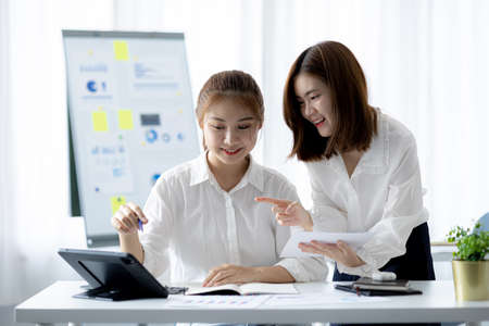 Atmosphere in the office of a startup company, two female employees are discussing, brainstorming ideas to working on summaries and marketing plans to increase sales and prepare reports to managers.の写真素材