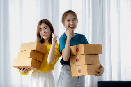 Two owners of an online store on the website are preparing parcels to send to customers following orders from the web page, they check the information and prepare for delivery to the customers.の写真素材