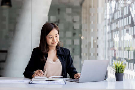 A beautiful Asian businesswoman sitting in her private office, she is checking company financial documents, she is a female executive of a startup company. Concept of financial management.の写真素材