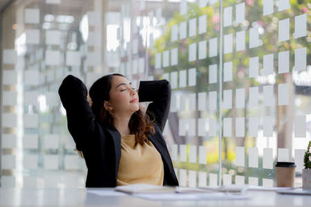 Working woman relaxing, a businesswoman in office, she is relaxing after working hard for a long time, causing fatigue and stress to take a break, she has office syndrome. Hard work concept.の写真素材