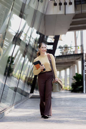Asian woman walking with book bag in university to attend class, female undergraduate student, female student walking into classroom. University education concept.の写真素材