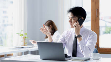 Startup company working atmosphere, male employee talking on the phone with customers, startup company operation by new generation. Concept of setting up and managing a startup company.の写真素材