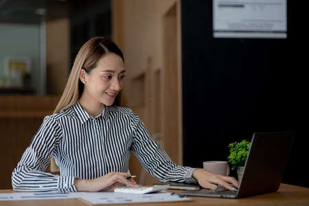 Beautiful Asian young woman looking at information on a laptop, concept image of Asian business woman working smart, modern female executive, startup business woman, business leader woman.の写真素材