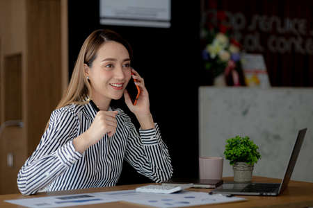 Asian woman talking on the phone, she is a salesperson in a startup company, she is calling customers to sell products and promotions. Concept of selling products through telephone channels.の写真素材