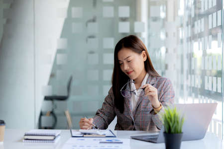 A beautiful Asian businesswoman sitting in her private office, she is checking company financial documents, she is a female executive of a startup company. Concept of financial management.の写真素材