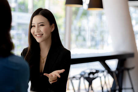 Atmosphere in the office of a startup company, two female employees are discussing, brainstorming ideas to working on summaries and marketing plans to increase sales and prepare reports to managers.の写真素材