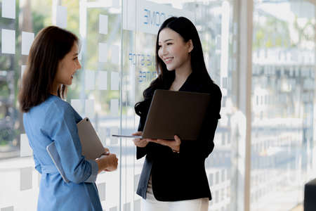 Atmosphere in the office of a startup company, two female employees are discussing, brainstorming ideas to working on summaries and marketing plans to increase sales and prepare reports to managers.の写真素材