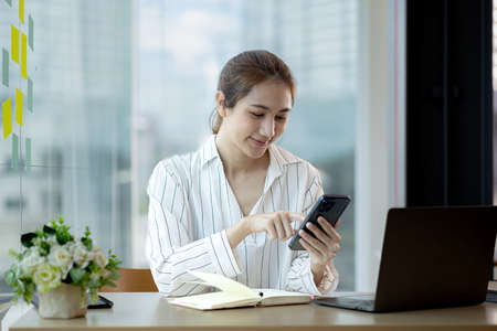 young businesswoman looking at financial information from a mobile phone, she is checking company financial documents, she is a female executive of a startup company. Concept of financial management.の写真素材