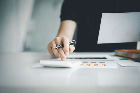 Businessman using a calculator to calculate numbers on a company's financial documents, he is...