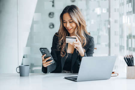 Beautiful woman holding a credit card, she uses a credit card to pay for goods and services online, the concept of using a credit card for online shopping, ordering goods and services on the website.の写真素材