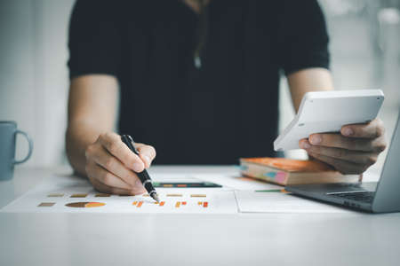 Businessman using a calculator to calculate numbers on a company's financial documents, he is...