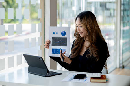 Asian woman working in office and discussing with business partner via laptop video call, young...