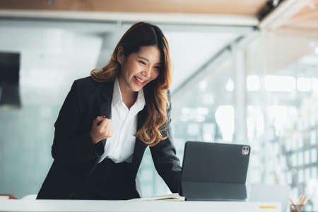 Woman gesturing and looking at tablet screen, businesswoman checking company monthly sales and pretending to be happy as sales meet planned targets according to policy. Sales management concept.の写真素材