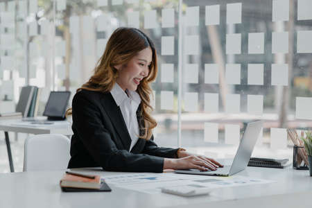 A businesswoman is checking company financial documents and using a laptop to talk to the chief financial officer through a messaging program. Concept of company financial management.の写真素材
