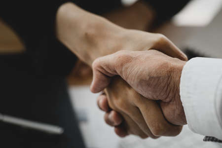 Close-up two business men holding hands, Two businessmen are agreeing on business together and shaking hands after a successful negotiation. Handshaking is a Western greeting or congratulation.の写真素材